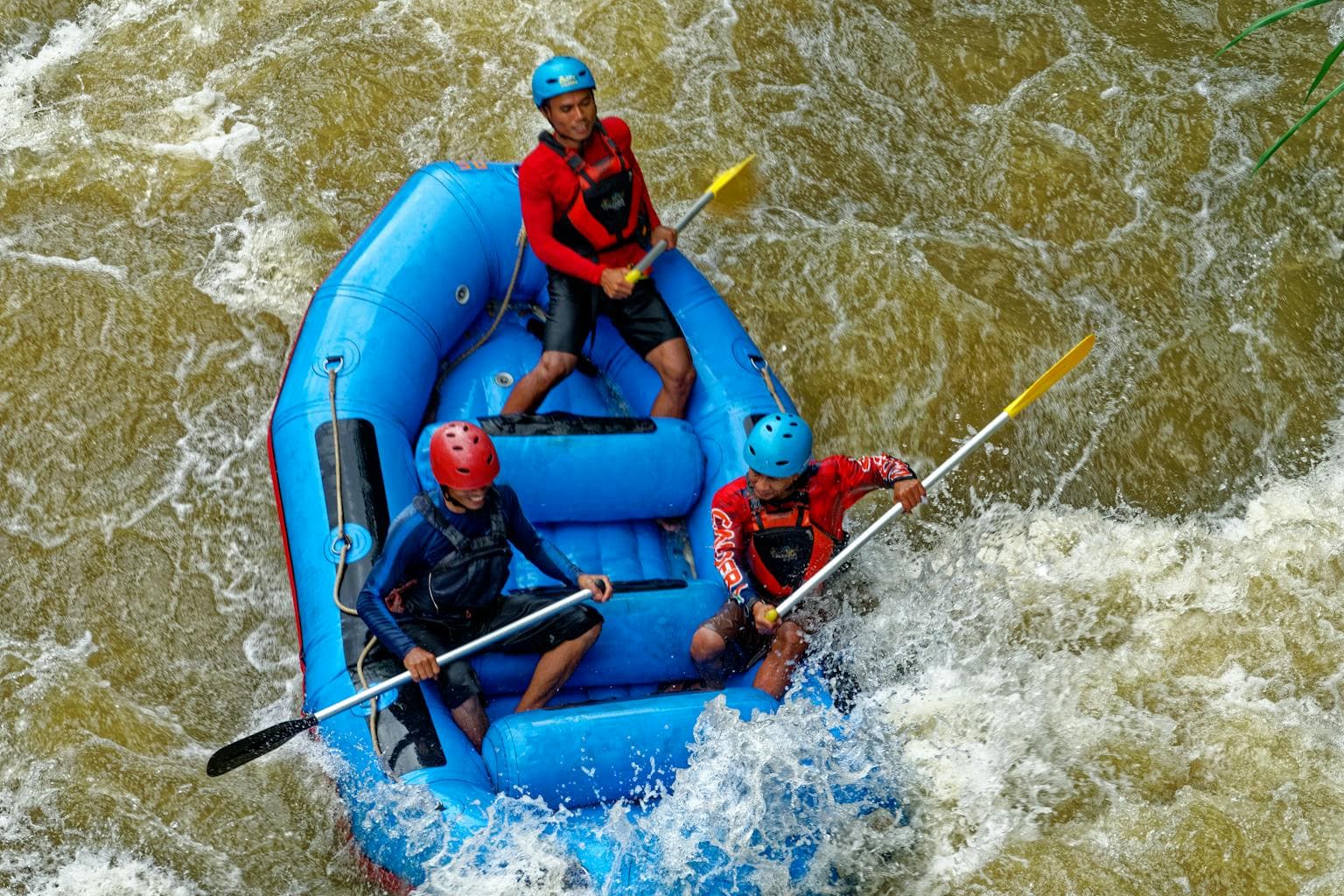 Three people white-water rafting through rapids in a blue inflatable raft